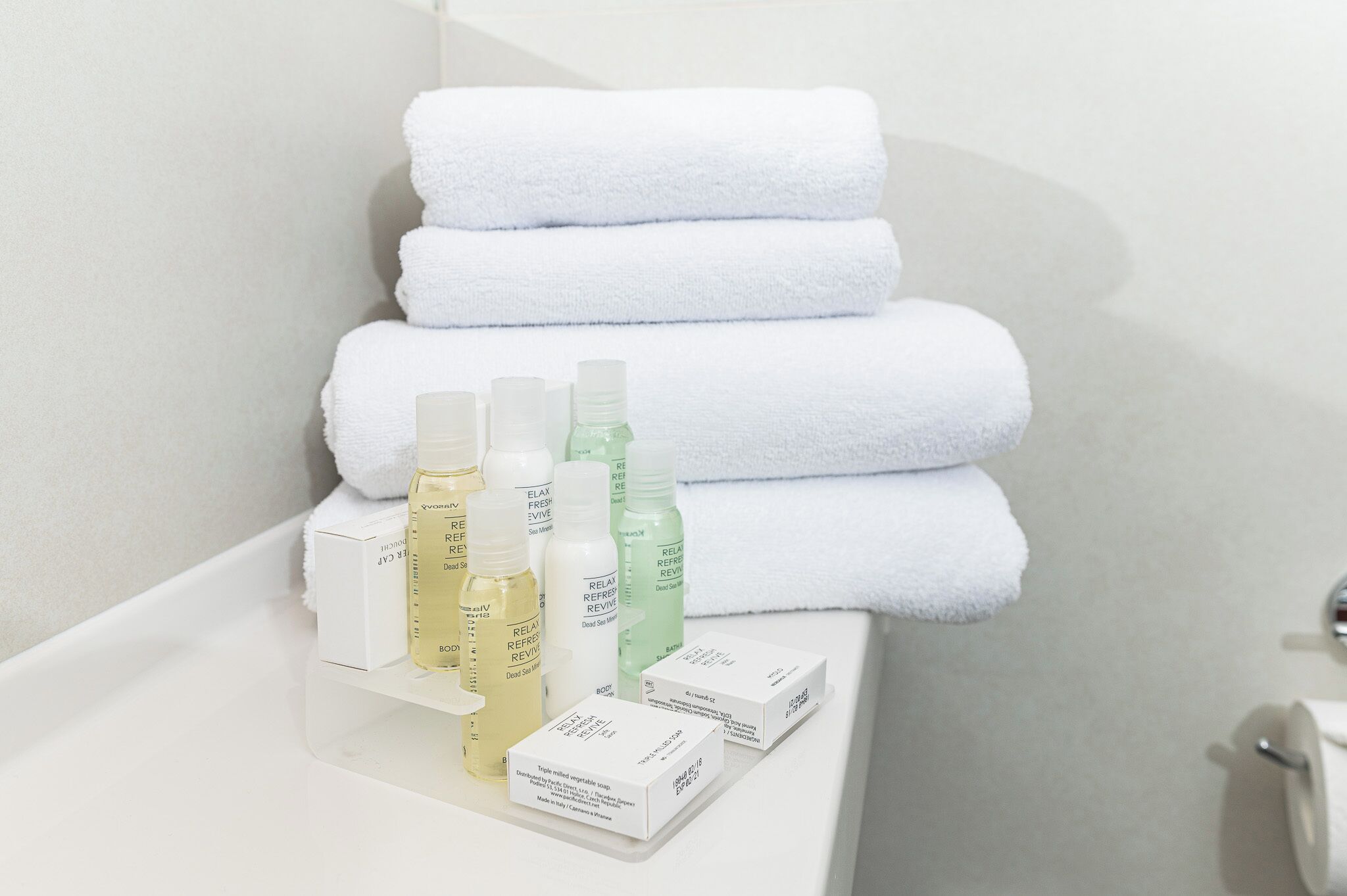A bathroom with stacked white towels, a white sink, and several bottles of bath products.