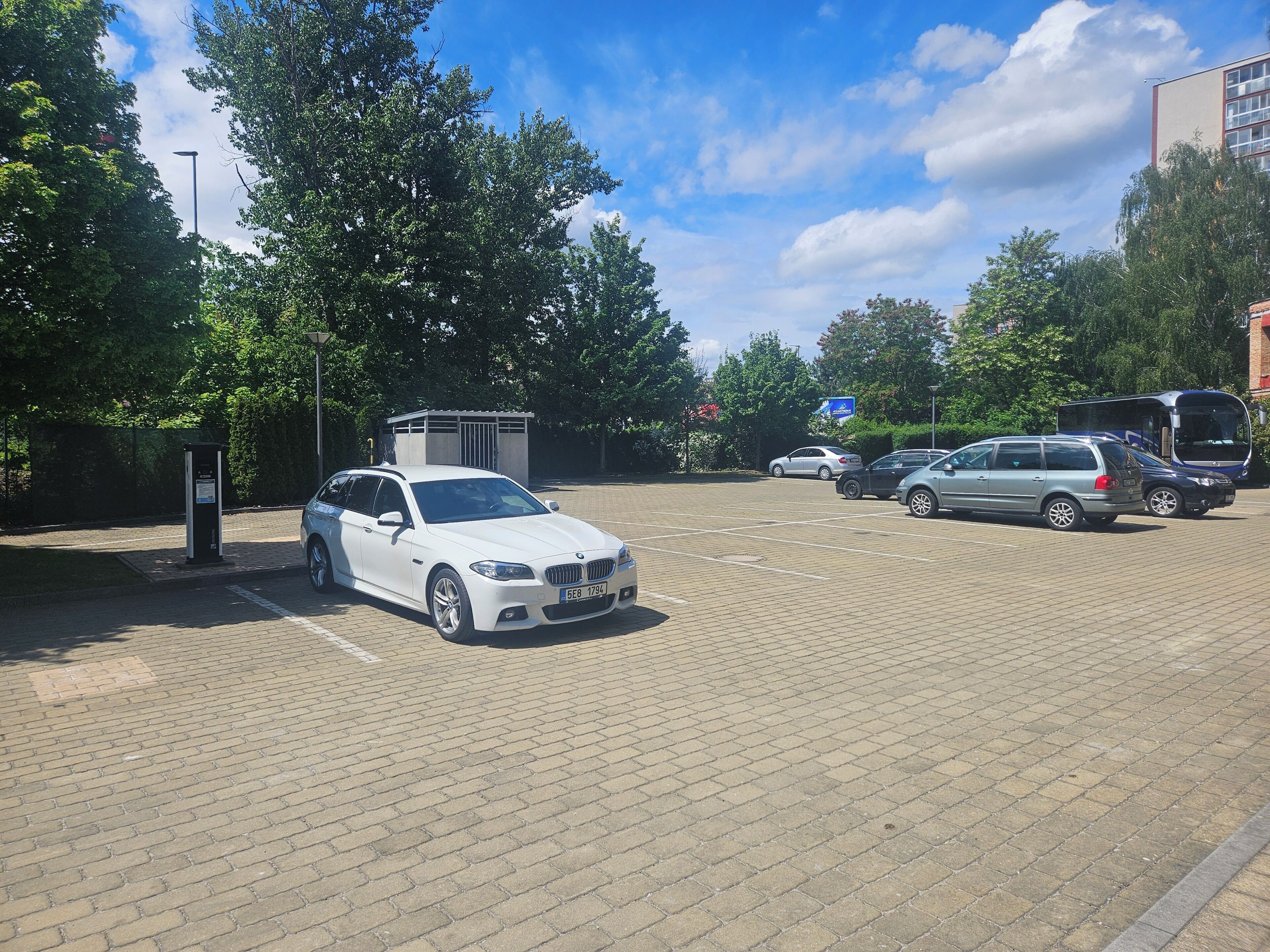 Un estacionamiento con un coche blanco, un autobús y un edificio al fondo.