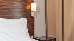 A hotel room with a wooden headboard, a bedside lamp, a small bedside table, and a bed with white bedding. - Hotel Euro (Pardubice)