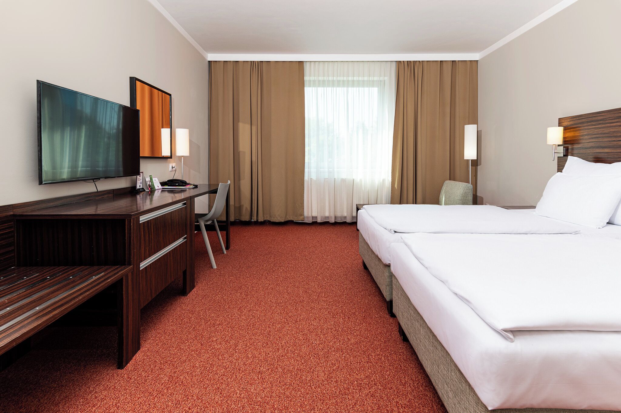 Habitación de hotel con cama, escritorio, silla, televisor y cortinas.