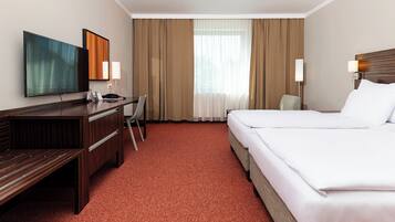 Habitación de hotel con cama, escritorio, silla, televisor y cortinas.