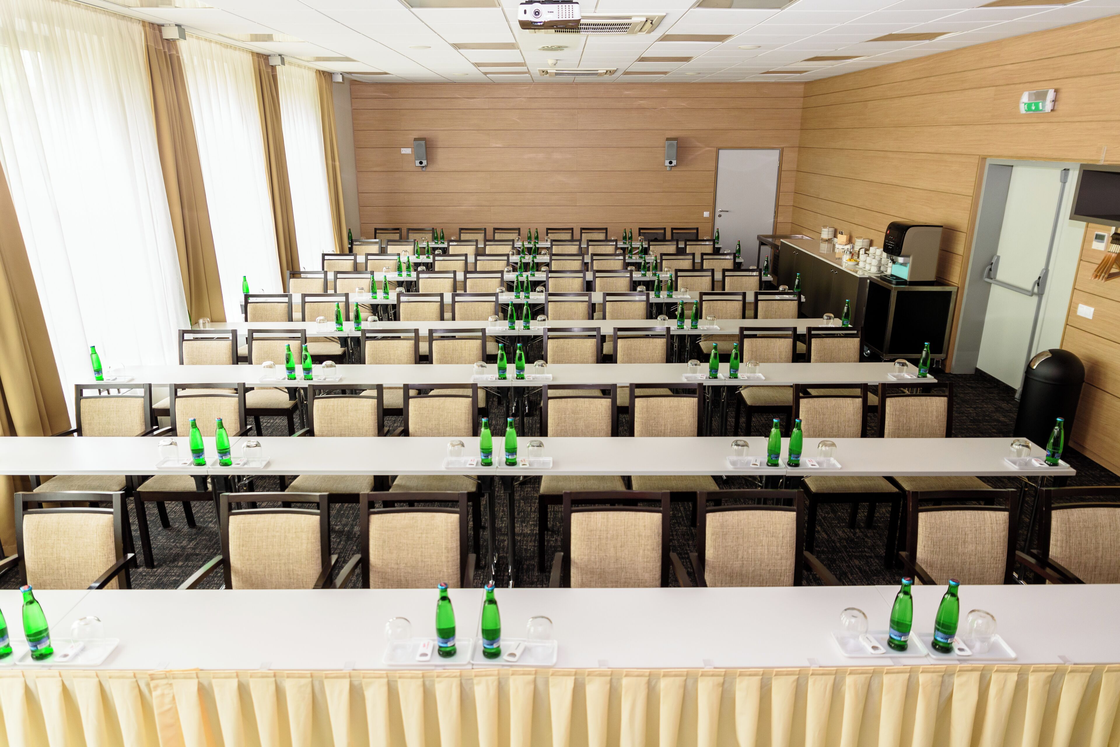 Une salle de conférence avec des rangées de tables, de chaises et des bouteilles vertes sur chaque table.