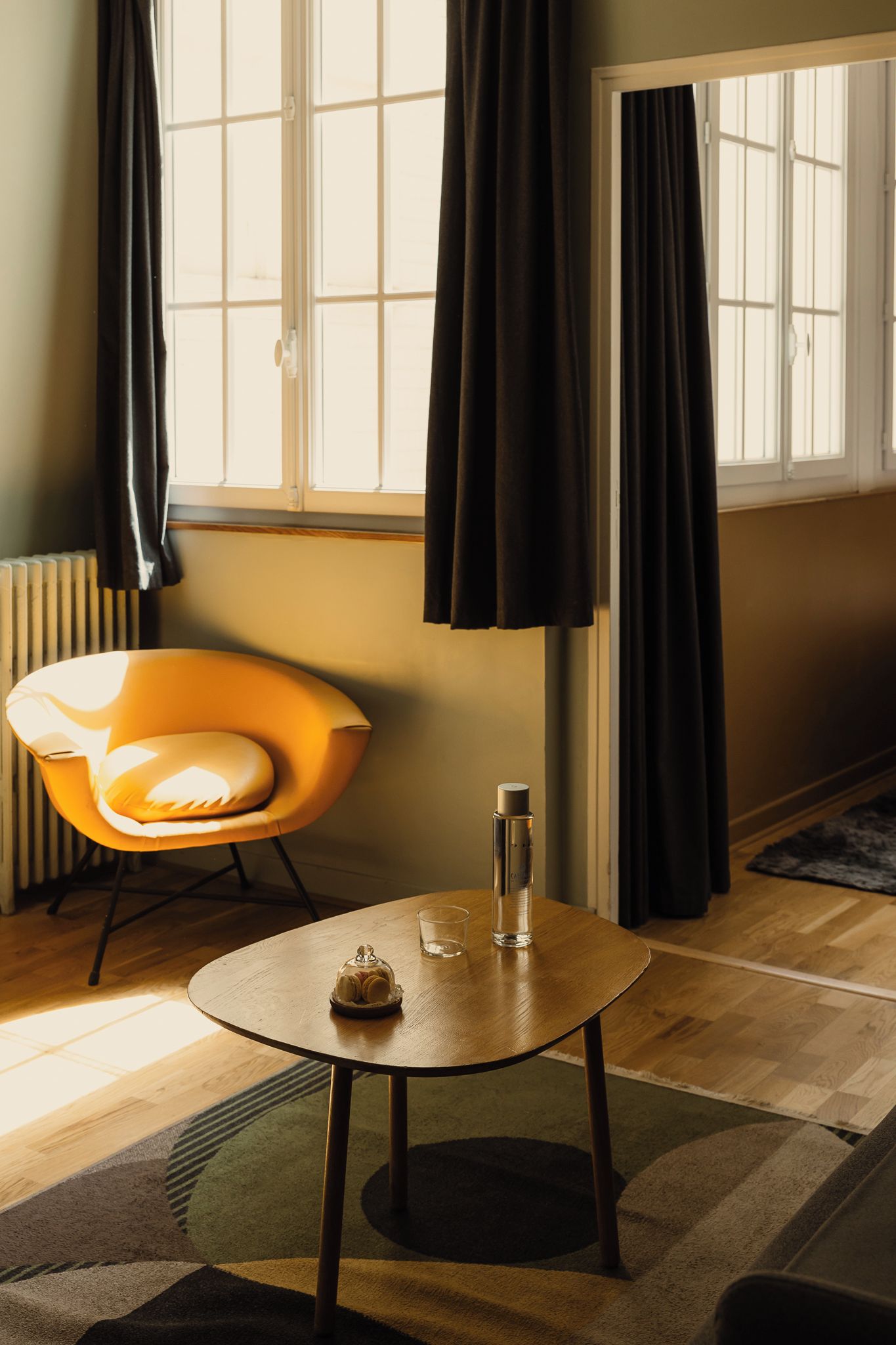 A room with a round table, a chair, a radiator, and a window with curtains.