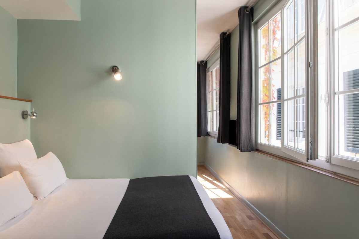 A bedroom with a bed, a bedside lamp, a window with curtains, and a view of the outside.