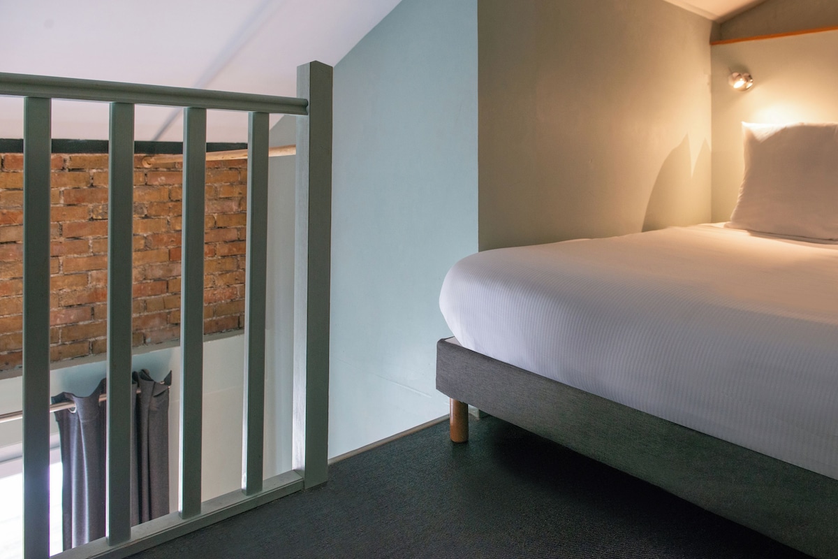 A modern hotel room with a bed, a view of a brick wall, and a balcony with metal railings.