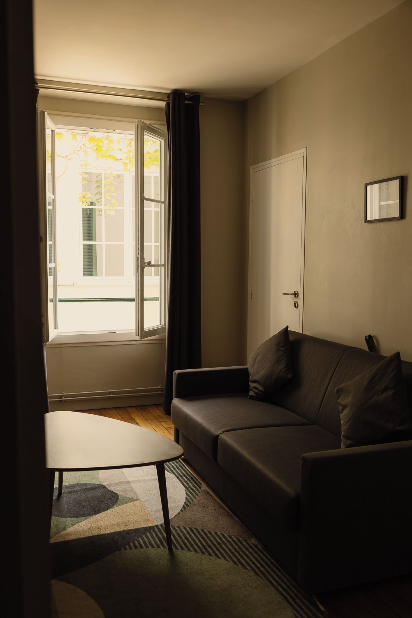 Ein Zimmer mit einer Couch, einem kleinen Tisch, einer Tür und einem fensterbepflanzten Fenster.