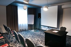 Una sala conferenze con uno schermo per proiettore, una lavagna e un tavolo con sedie.