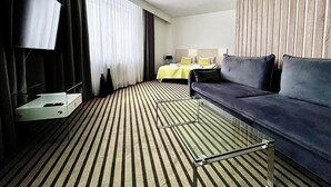 A hotel room with a striped carpet, a sofa, a bed with a yellow bedspread, a TV mounted on the wall, and a window with curtains. - NoBo Hotel (Lodz)