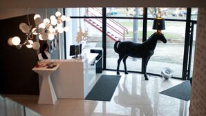 A reception area with a modern desk, a horse statue, and a large window with a view of the outside. - NoBo Hotel (Lodz)