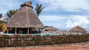 Un complexe hôtelier doté de bâtiments à toits de chaume, d’une piscine et offrant une vue sur la mer.