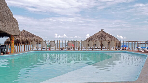 A pool area with thatched umbrellas, lounge chairs, and a wooden fence. - Las Cabanas Del Capitan (Rincón de Guayabitos)
