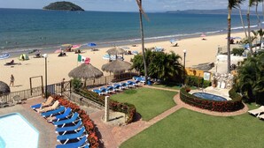 A beach resort with a swimming pool, lounge chairs, and a view of the ocean. - Las Cabanas Del Capitan (Rincón de Guayabitos)