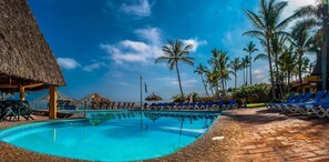Una piscina con sillas de descanso y palmeras al fondo.
