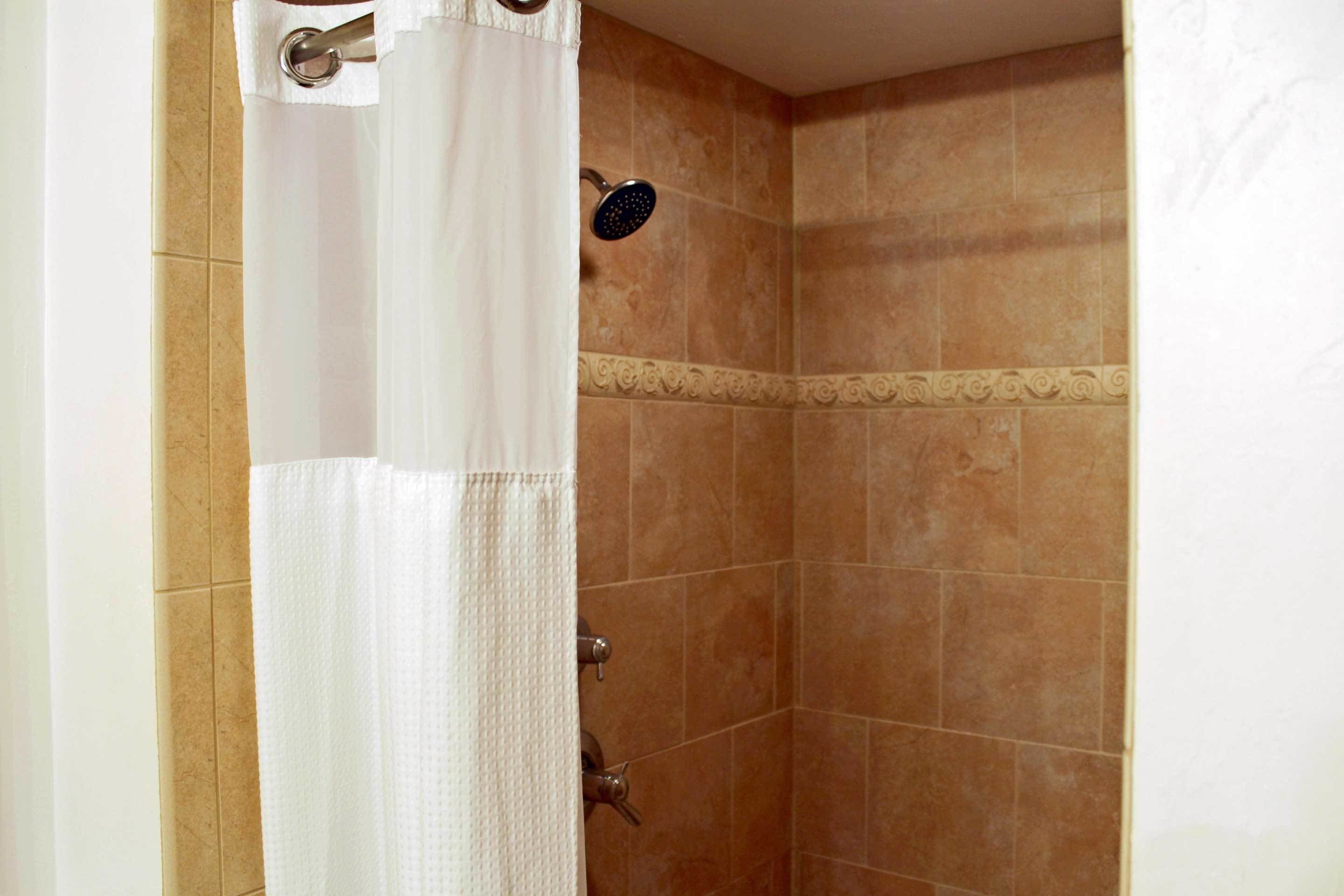 A shower area with beige tiles and a white shower curtain.