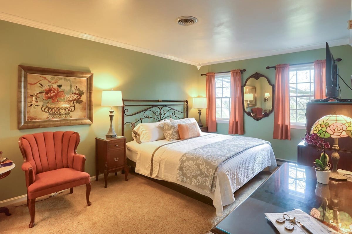A bedroom with a bed, bedside tables, a chair, a desk, and a window with curtains.
