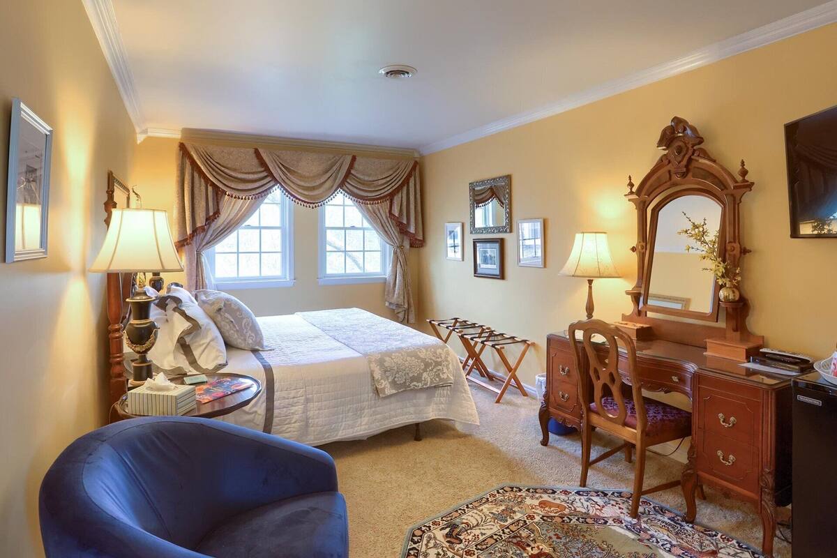 A hotel room with a bed, a desk, a chair, a dresser, and a large mirror.