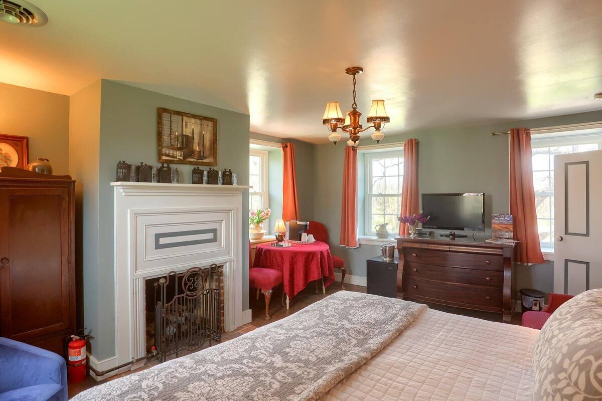 A hotel room with a fireplace, a bed, a desk with a television, and a window with curtains.