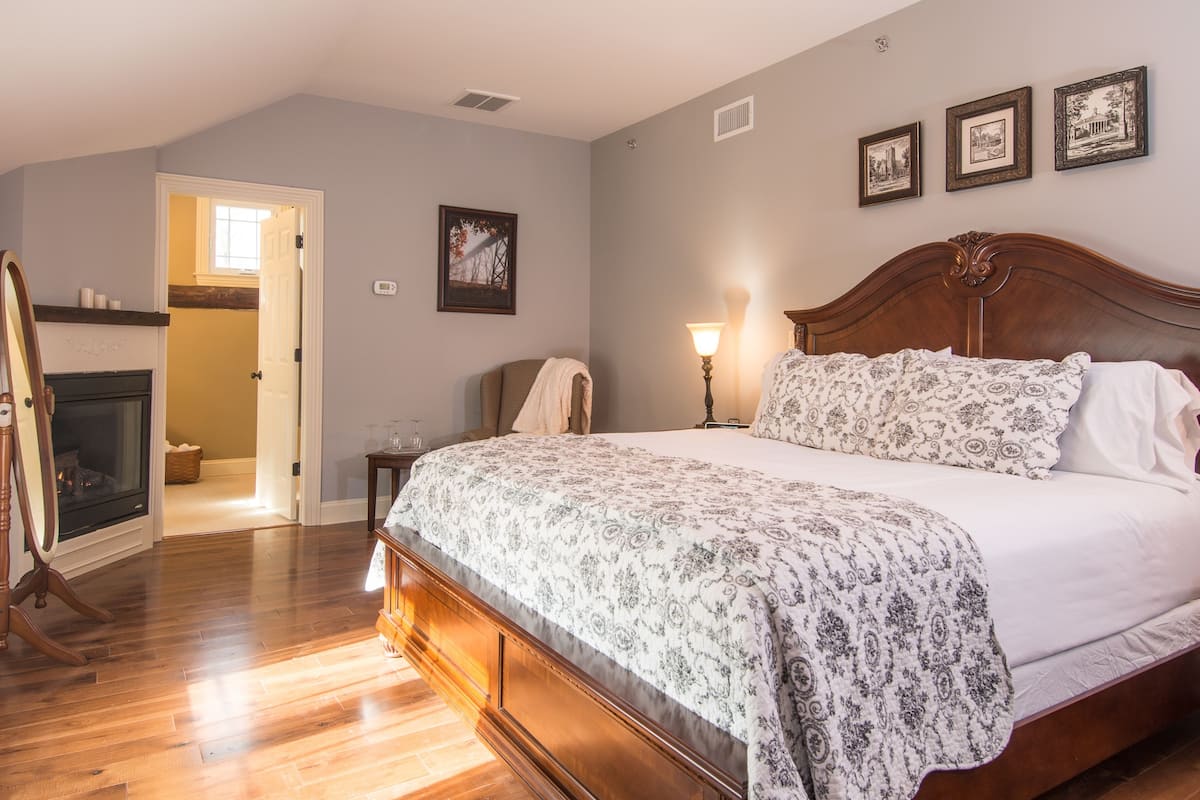 A bedroom with a large bed, a wooden headboard, a fireplace, and a door leading to another room.