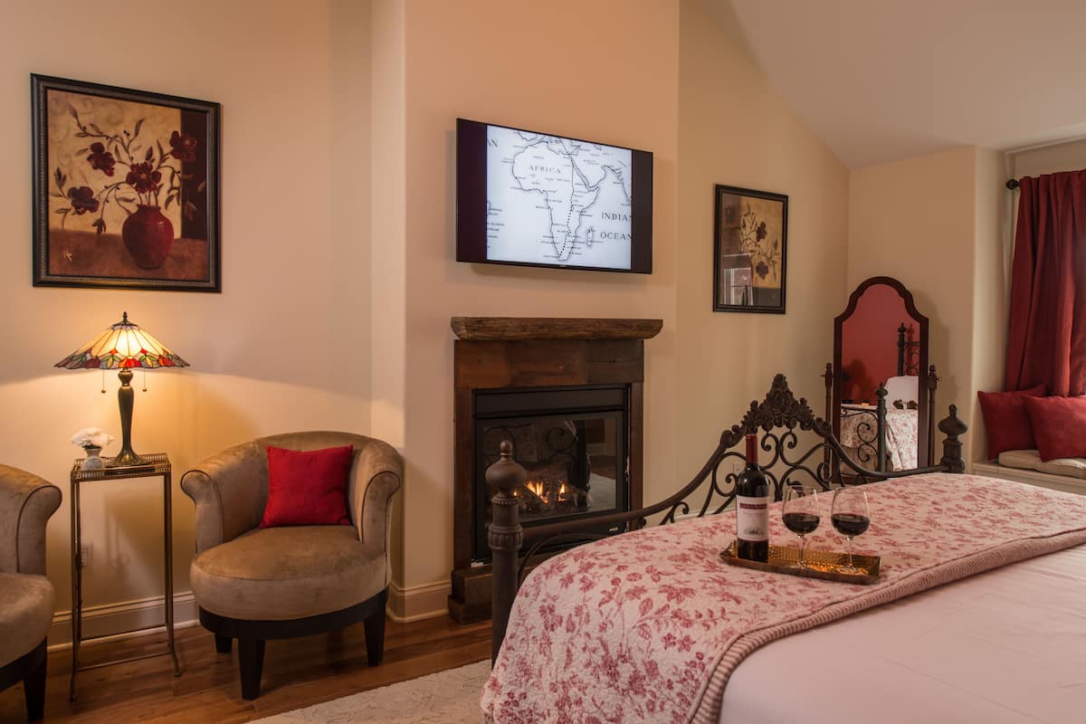 A bedroom with a fireplace, a bed with a floral bedspread, a map on the wall, and a lamp.