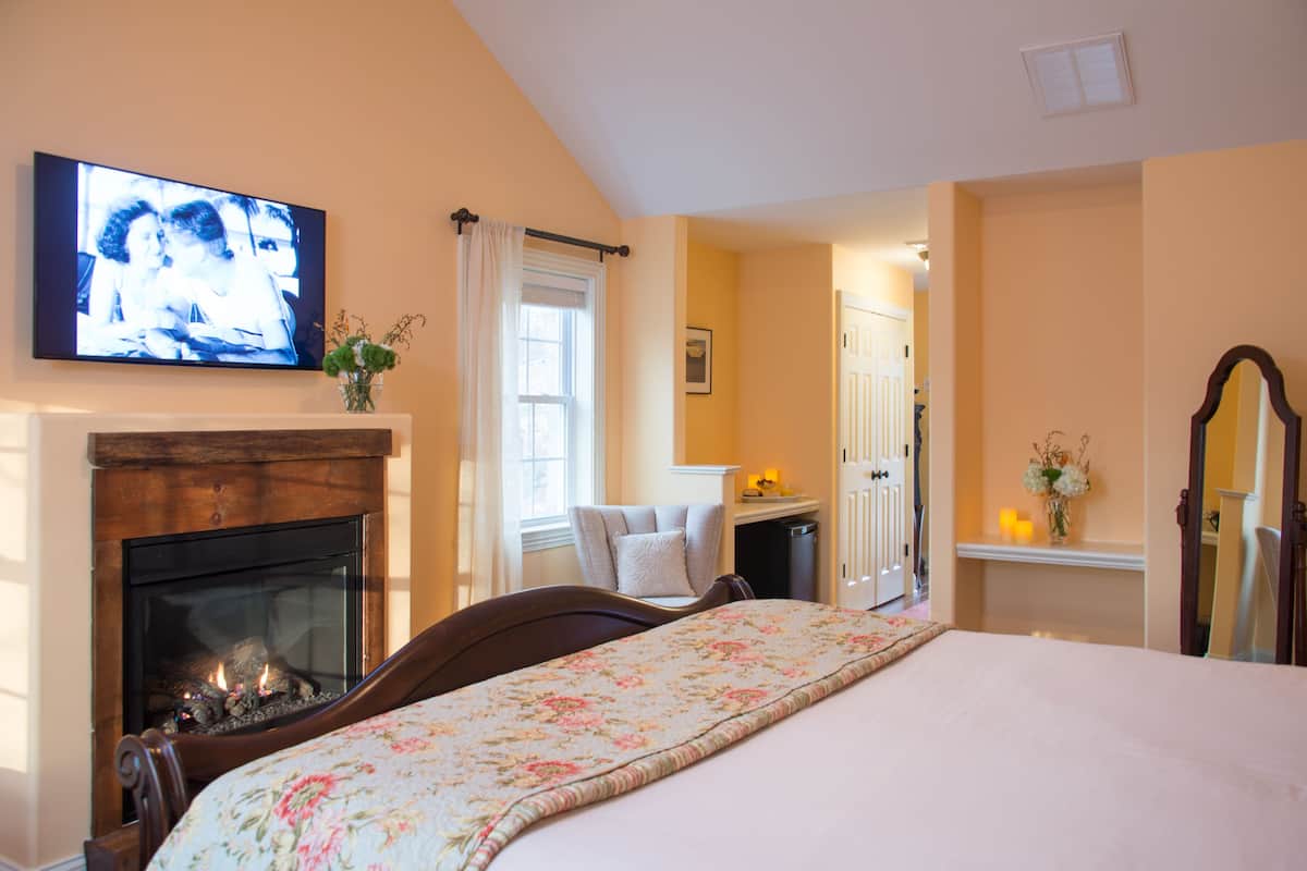 A bedroom with a fireplace, a bed with a floral bedspread, a television mounted above the fireplace, and a mirror on the wall.