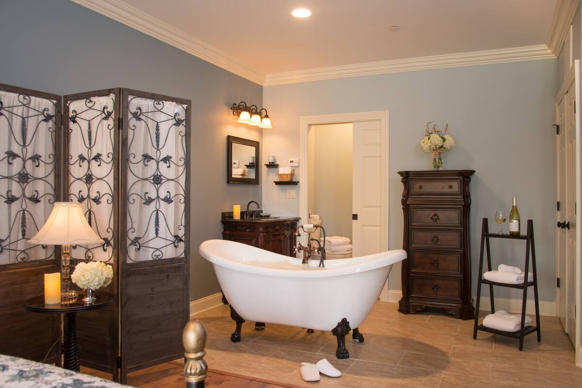 A bathroom with a freestanding bathtub, a vanity with a mirror, a wooden cabinet, and a towel rack.