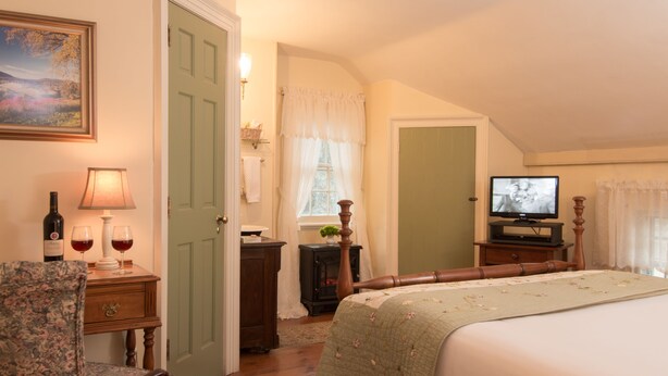 A bedroom with a bed, a chair, a television, and a window with curtains.