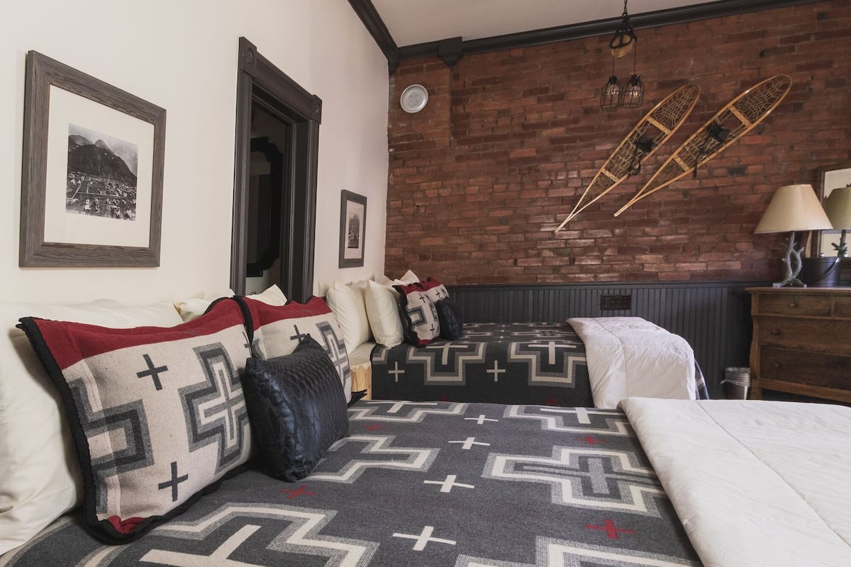 Una habitación con dos camas, un aparador de madera, un espejo y una pared de ladrillo.