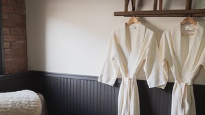 Two white robes hanging on a wooden rack in a room with dark wooden paneling and a brick wall. - Teller House (Silverton)