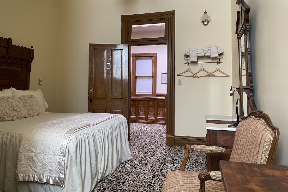Un dormitorio con una cama grande, una puerta de madera, una silla, una mesa y una lámpara colgante.