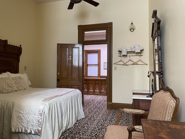 A bedroom with a large bed, a wooden door, a chair, a table, and a hanging light fixture. - Teller House (Silverton)
