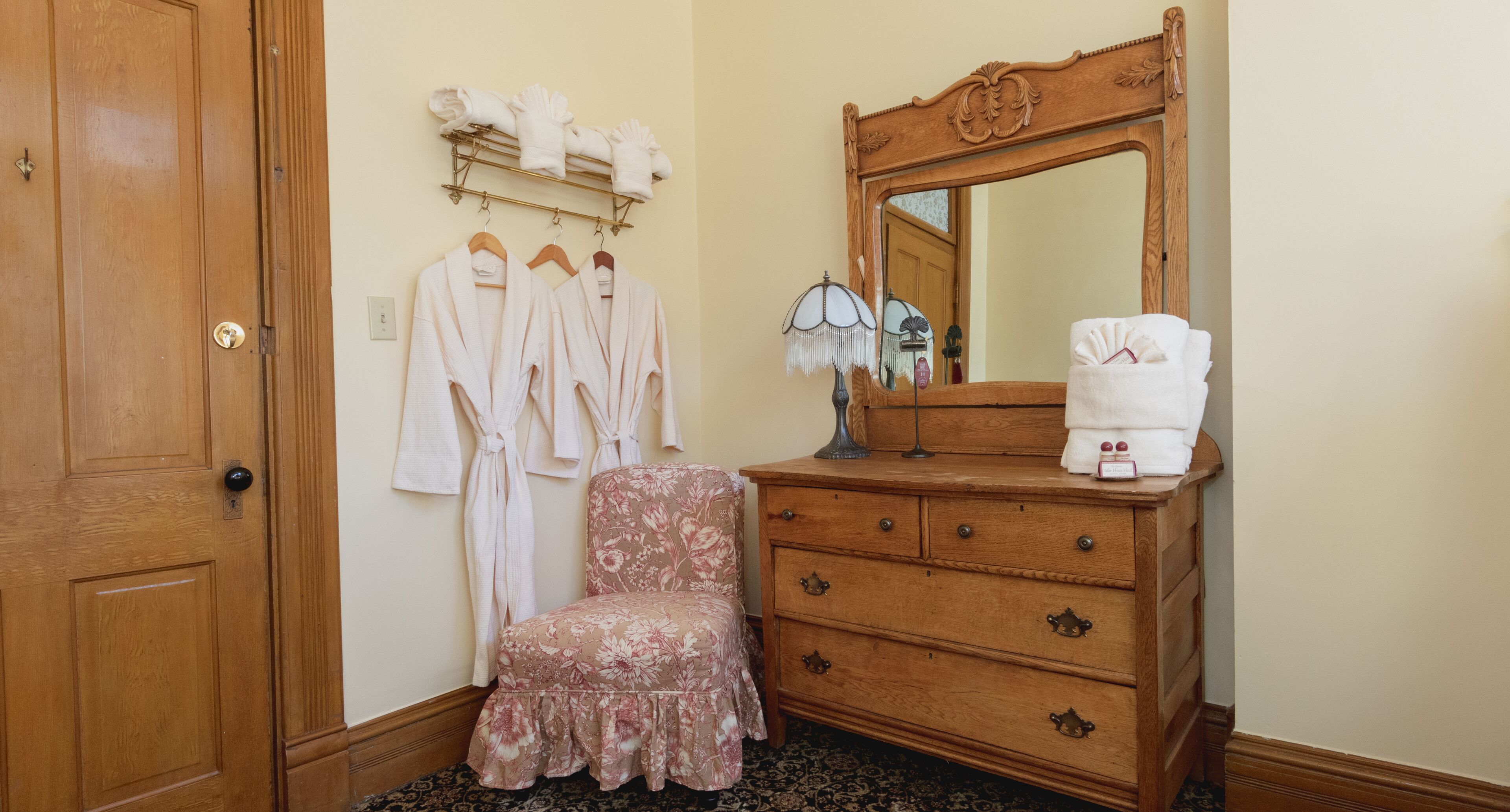Une commode en bois avec un miroir, une chaise à motifs floraux et une porte en bois.