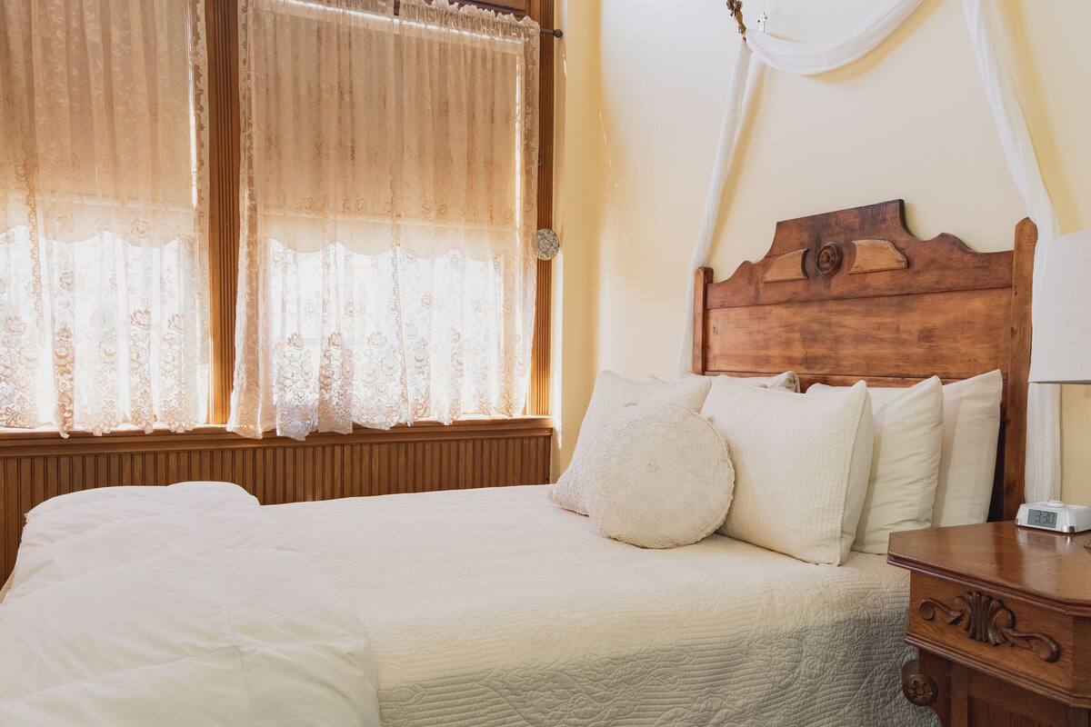 Una cama bien hecha con ropa blanca, un cabecero de madera y una mesita de noche con una lámpara.