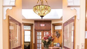 A hallway with a red carpet, wooden furniture, a chandelier, and framed artwork. - Teller House (Silverton)