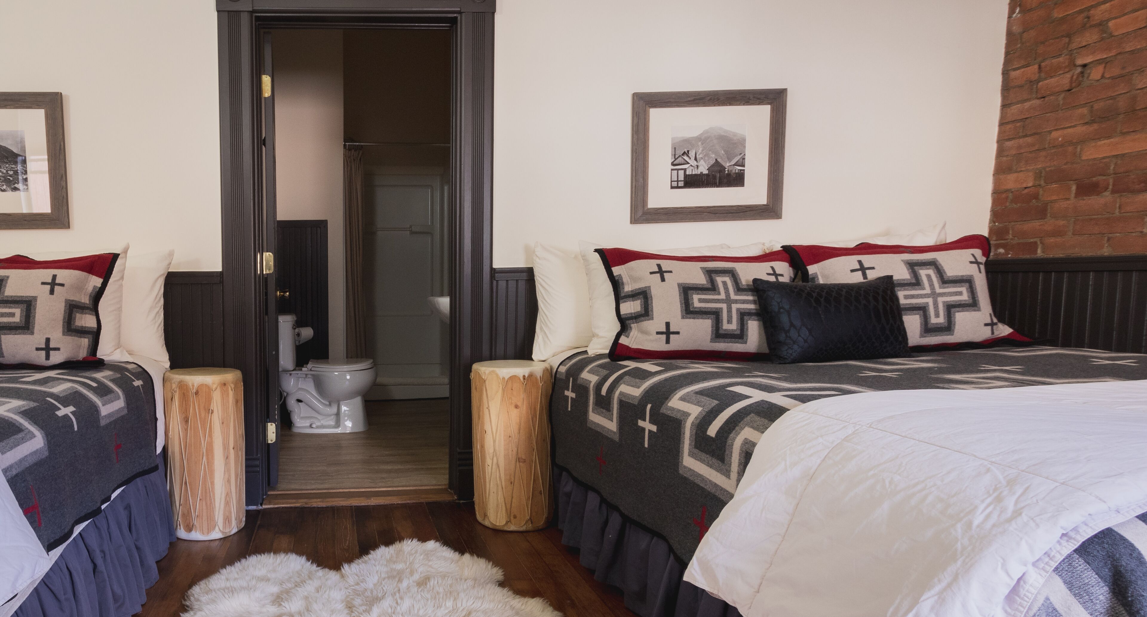 A bedroom with two beds, a wooden stool, a white fluffy rug, and a framed picture on the wall.