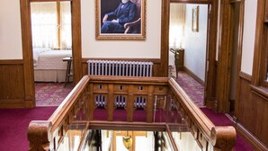A grand staircase with a wooden handrail, a radiator below, and a framed portrait on the wall. - Teller House (Silverton)