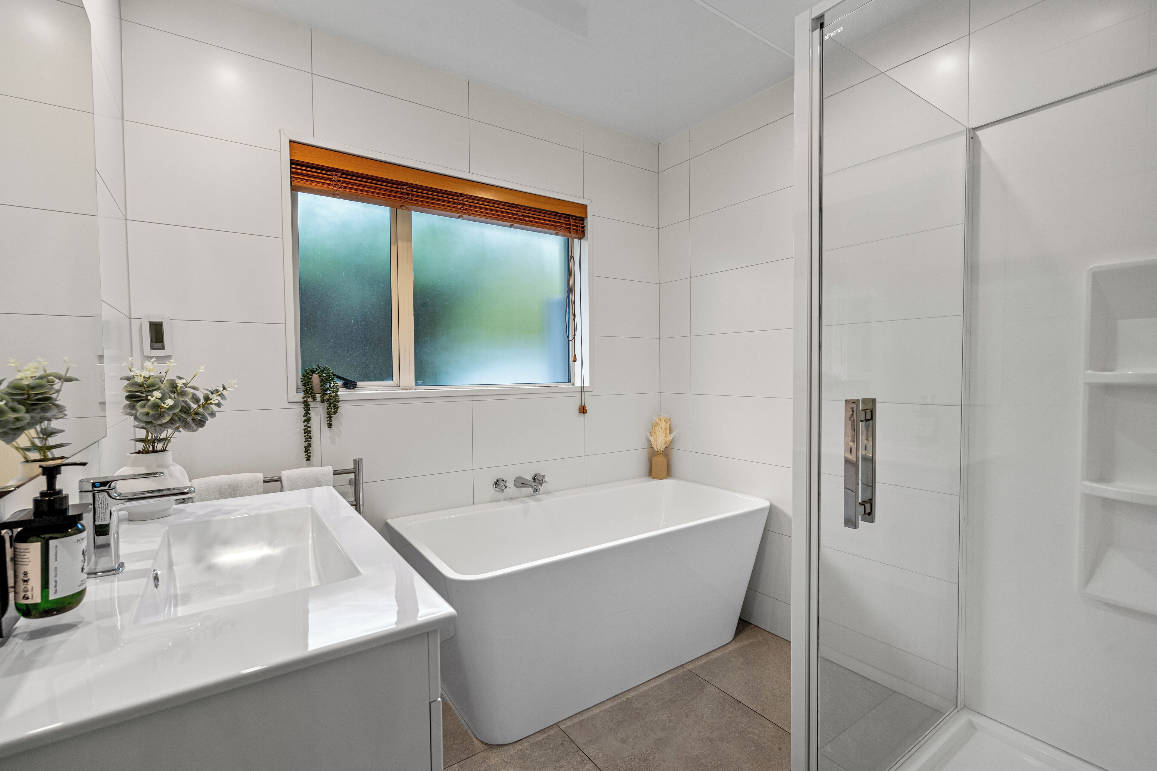 A modern bathroom with a freestanding bathtub, a glass shower enclosure, and a window with blinds.