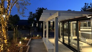A modern outdoor patio area with a glass enclosure, wooden benches, and string lights. - Tasman Holiday Parks - Christchurch (Christchurch)