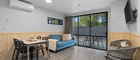 A modern living room with a dining area, a sofa, and a TV mounted on the wall.