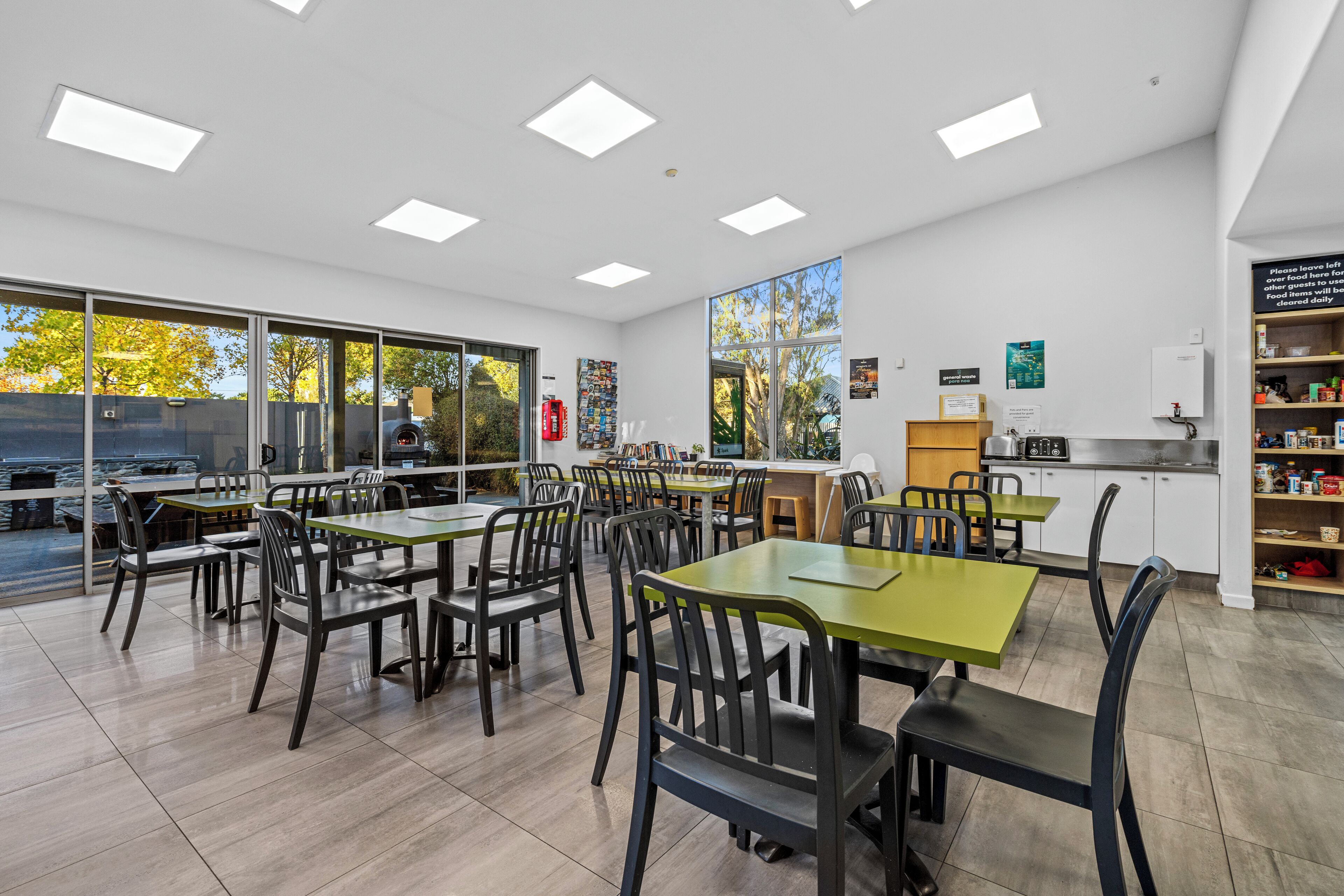 Un comedor moderno con varias mesas y sillas, ventanas amplias y una zona de cocina.