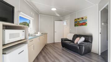 A compact kitchen with a microwave, a sink, and a window. There is a black leather sofa with cushions and a painting of a car on the wall.