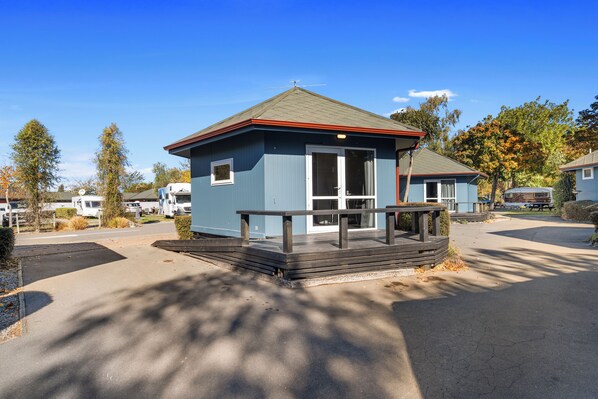A small, single-story building with a blue exterior and a red roof, featuring a wooden deck and a picnic table.