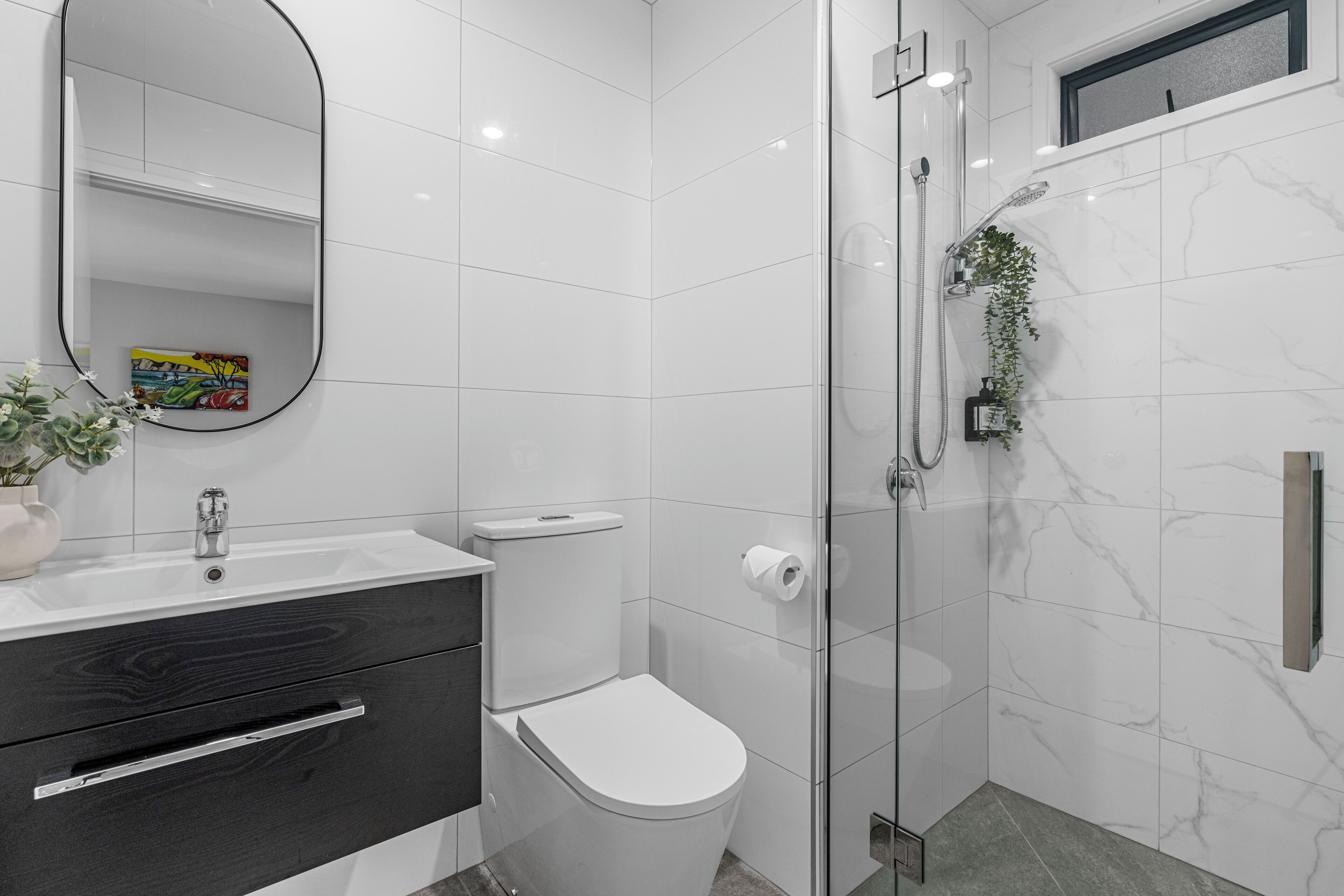A modern bathroom with a white toilet, a sink with a mirror, and a shower area.