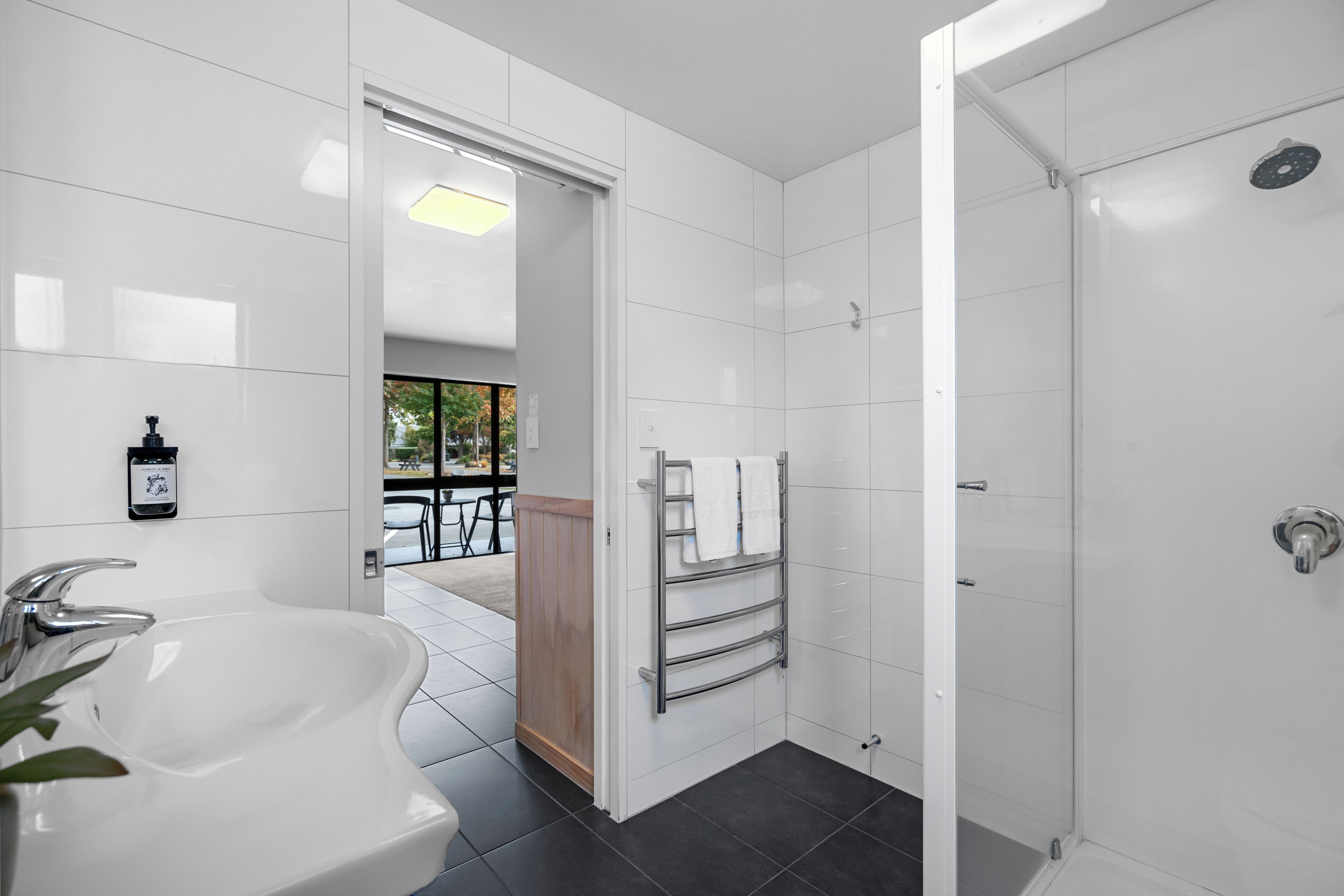 A modern bathroom with a large white sink, a glass shower enclosure, and a towel rack.