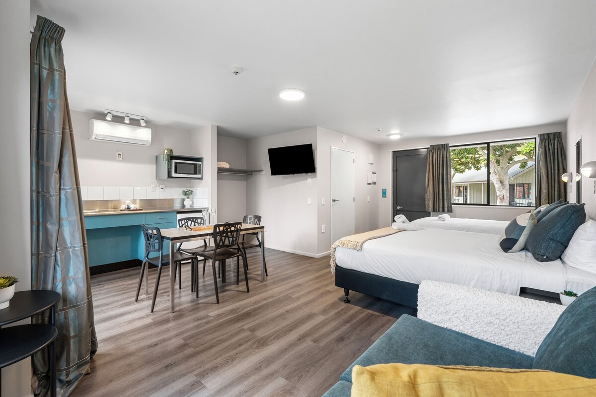 Ein modernes Hotelzimmer mit Küchenzeile, Essbereich und zwei Betten.