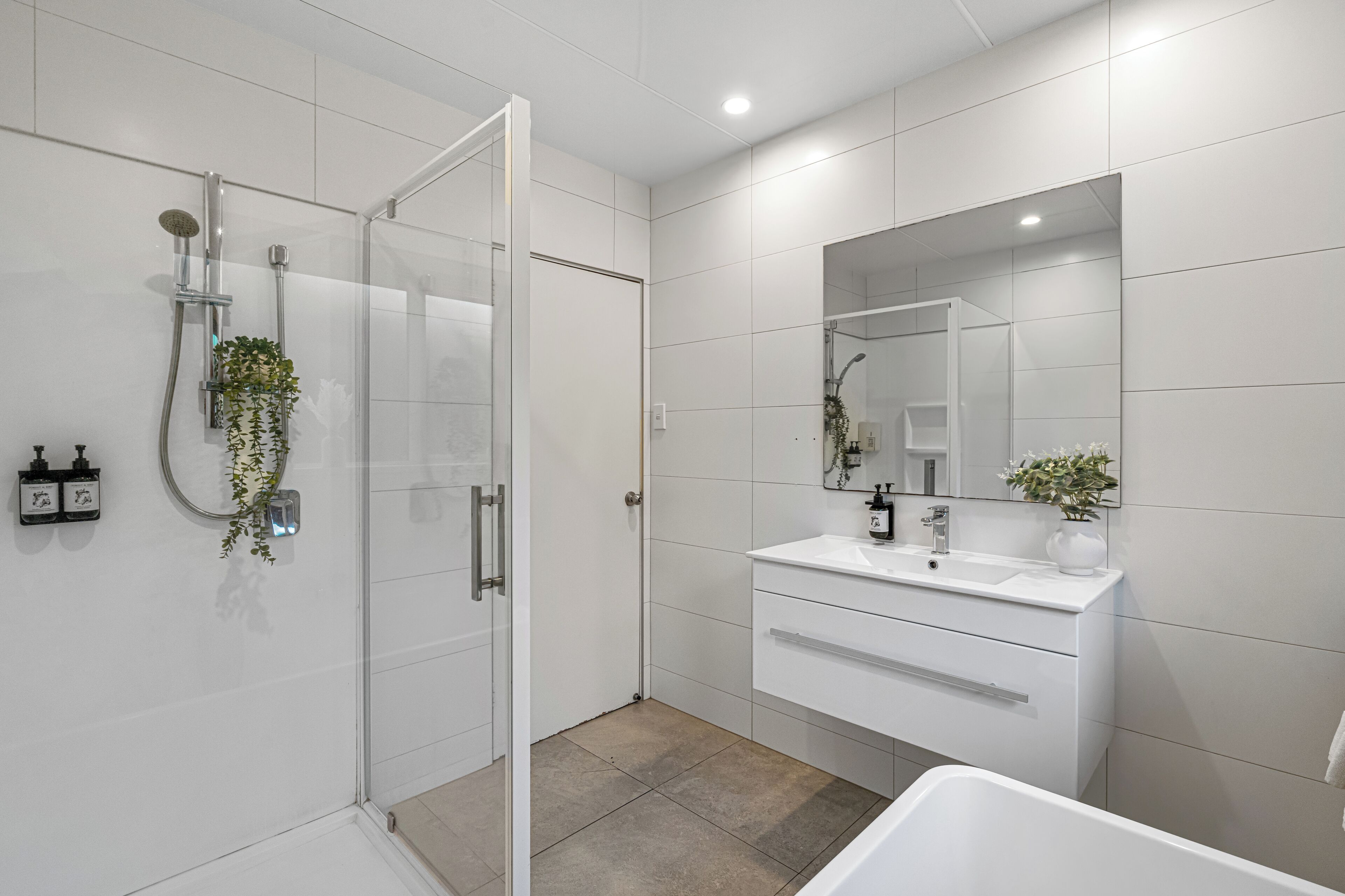 A modern bathroom with a glass-enclosed shower, a white vanity with a mirror, and a bathtub.