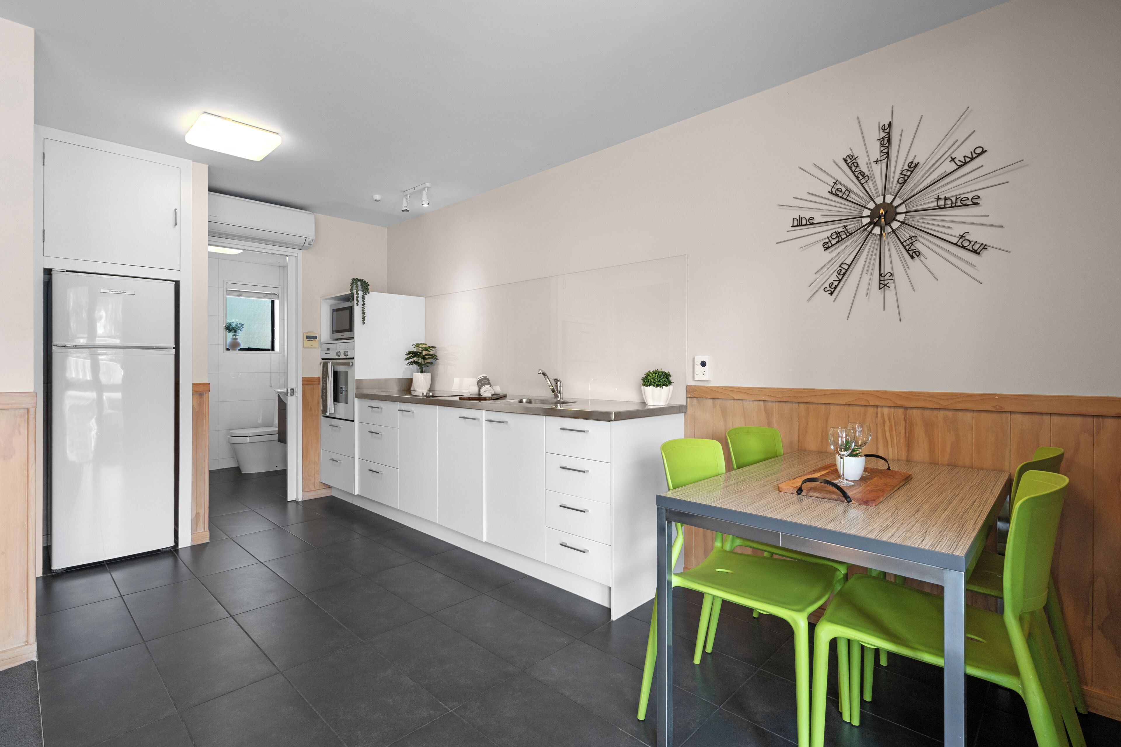Una cocina moderna con armarios blancos, una mesa de comedor de madera y sillas verdes.