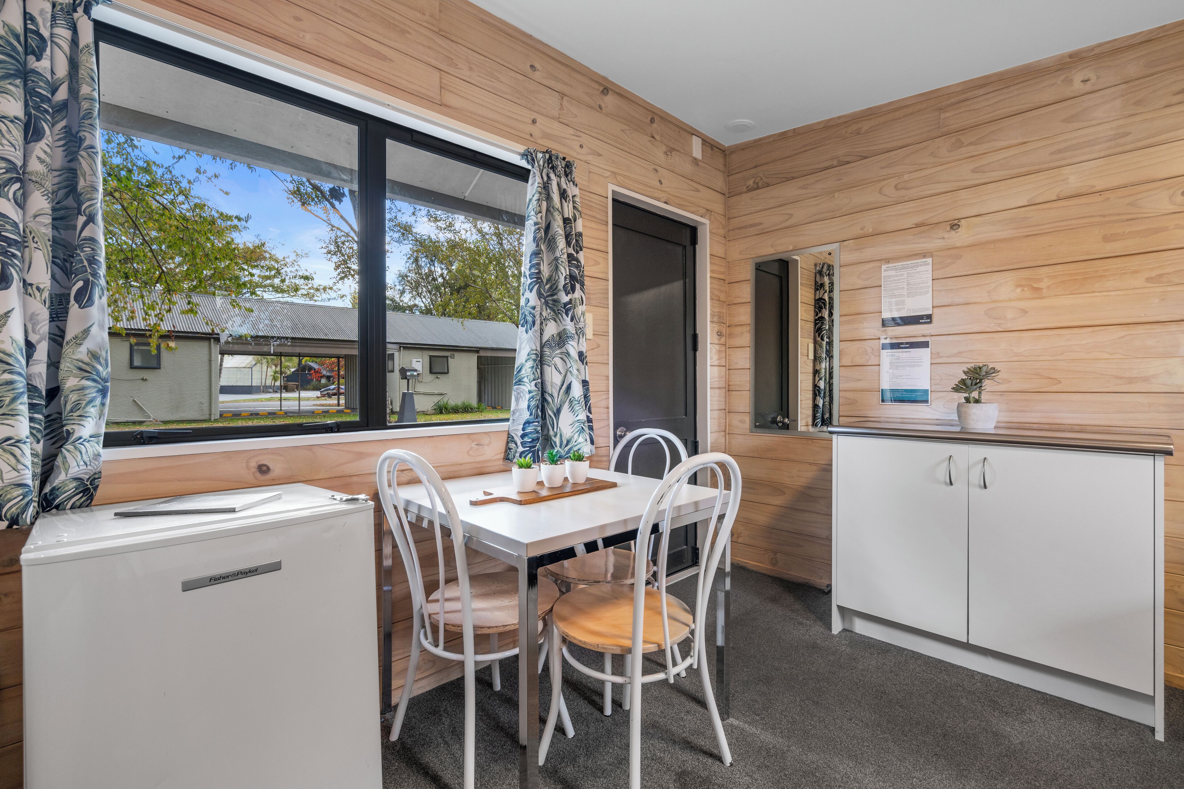 Una cocina compacta con detalles de madera, un refrigerador blanco, una mesa de comedor con sillas y un mueble pequeño.