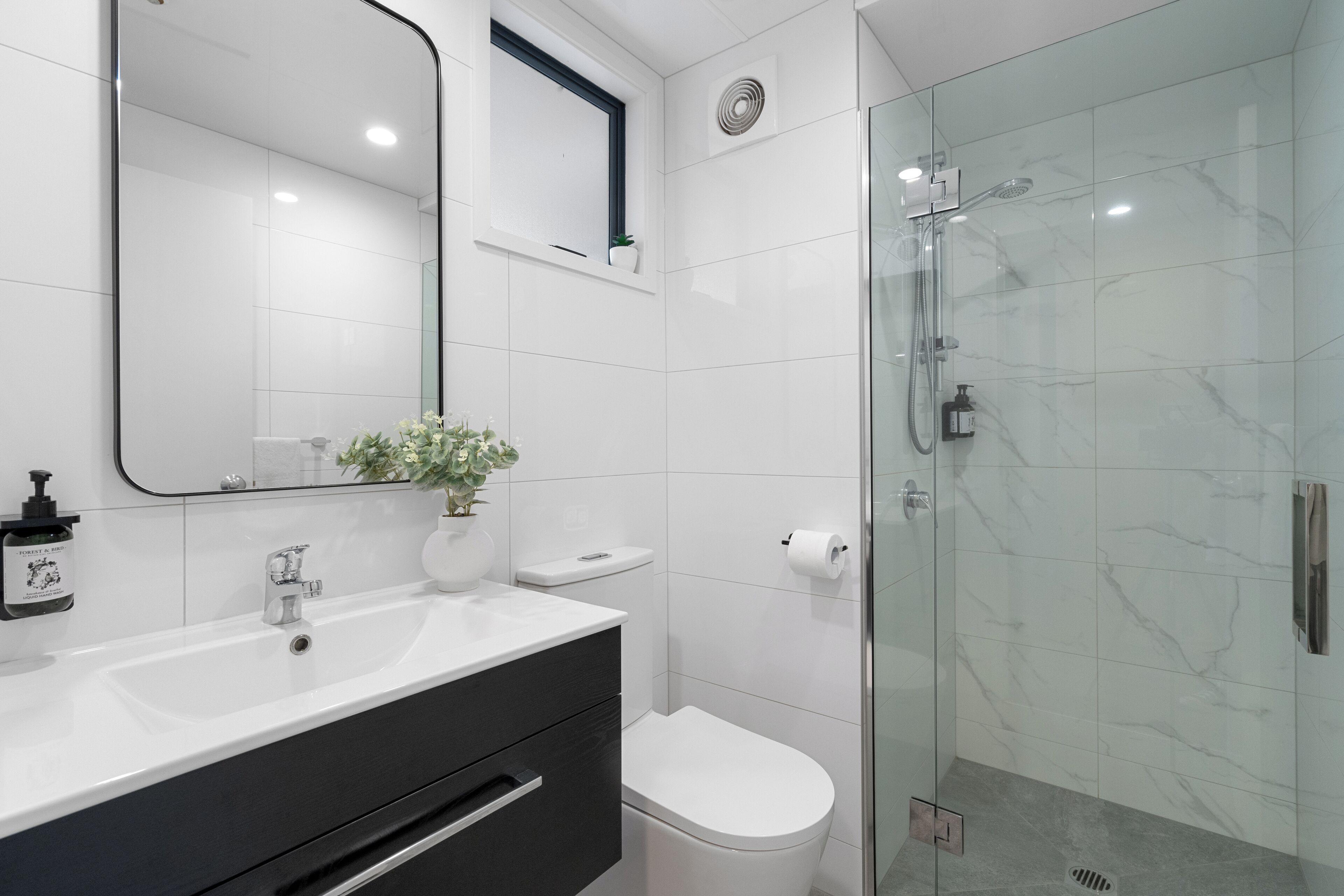 A modern bathroom with a white sink, black vanity, white toilet, and a glass-enclosed shower.