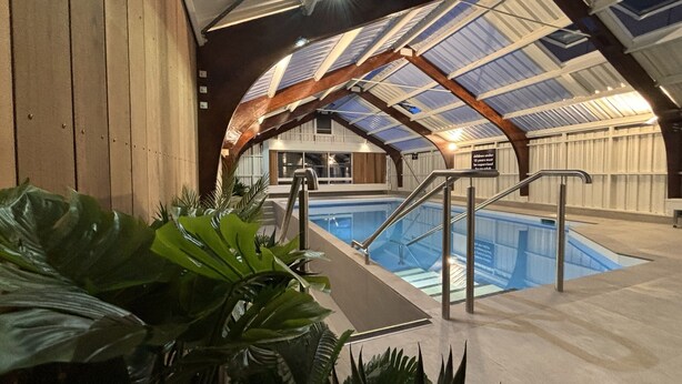 An indoor swimming pool with a high ceiling and skylights, surrounded by wooden walls and potted plants. - Tasman Holiday Parks - Christchurch (Christchurch)
