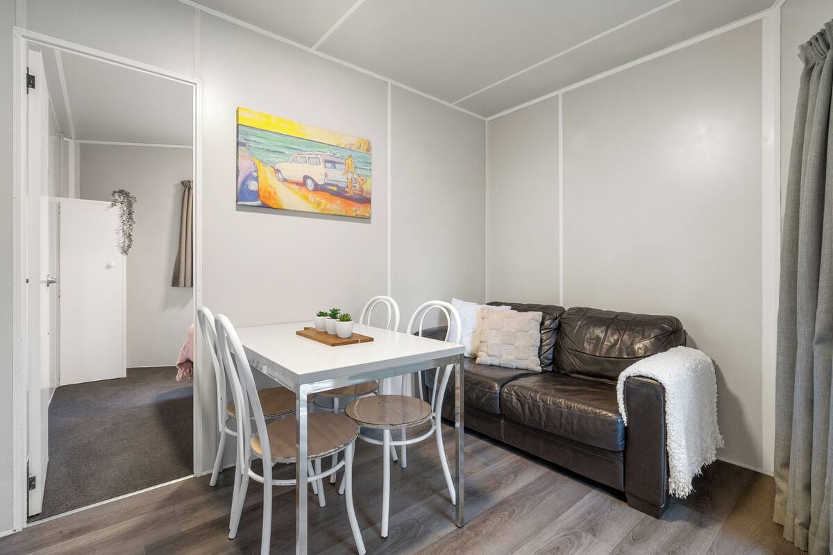 Un espacio habitable compacto con una mesa de comedor, sillas, un sofá y un cuadro en la pared.